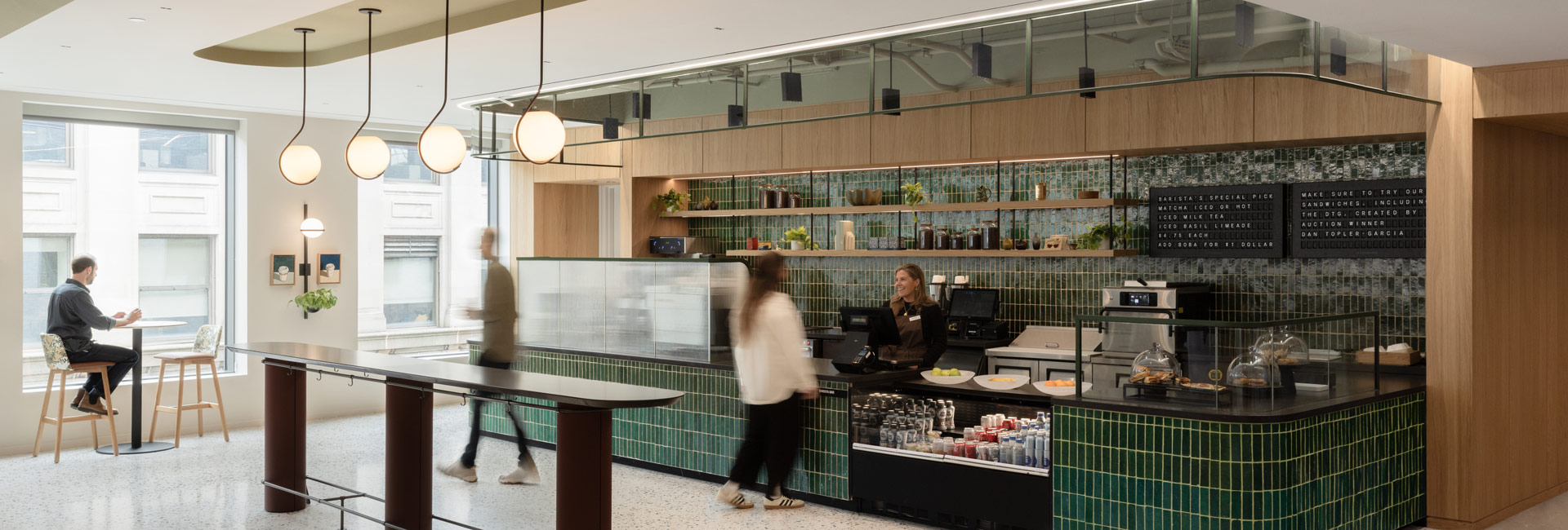 Bain & Company café with green tile, wood finishes, pendant lights, bar seating, and employees gathering near the counter.