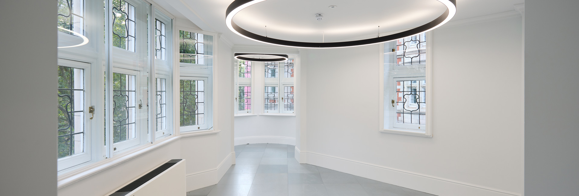 Bright, curved room with decorative windows, gray tile flooring, and large circular pendant lights.