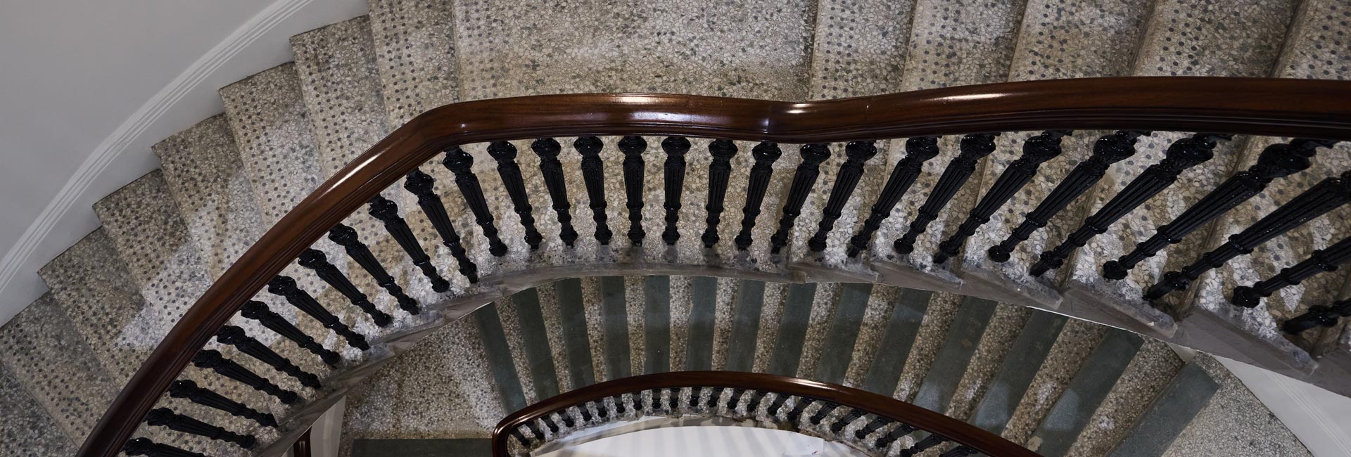 Overhead view of a curved terrazzo staircase with ornate black balusters and a polished wood handrail.