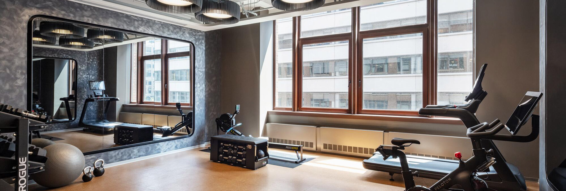 Office fitness center equipped with treadmills, stationary bikes, rowing equipment, weights, and a wall mirror.