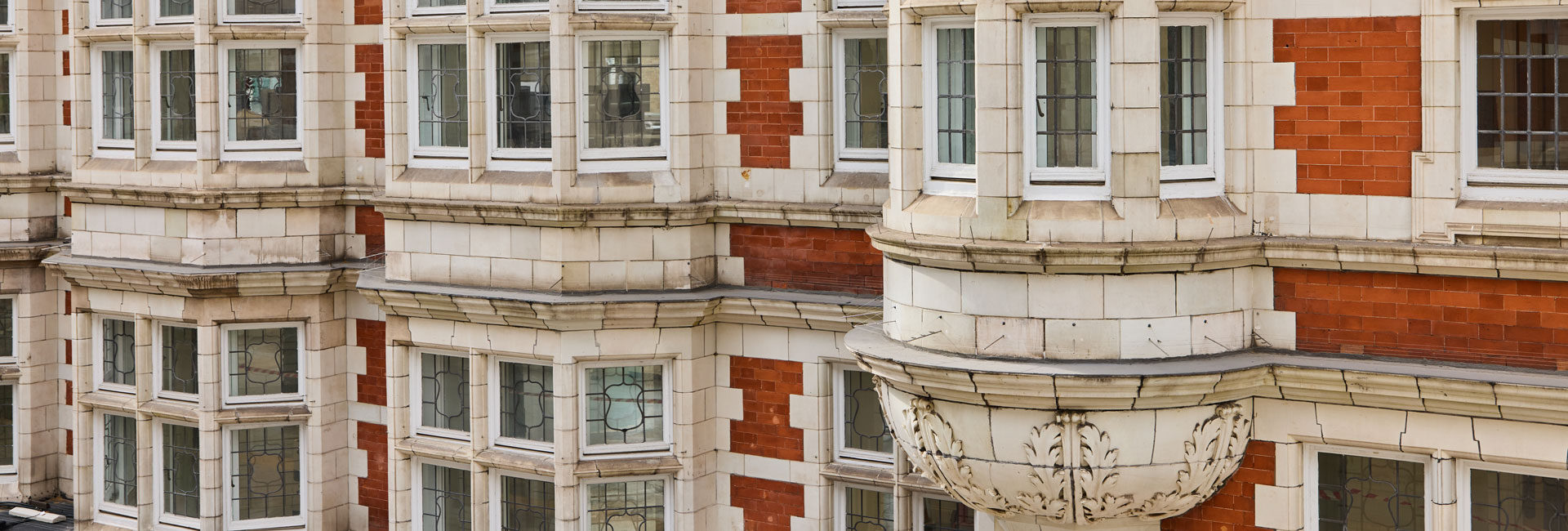 Historic red-brick and white-stone façade featuring bay windows with decorative leaded glass and ornate carved detailing.