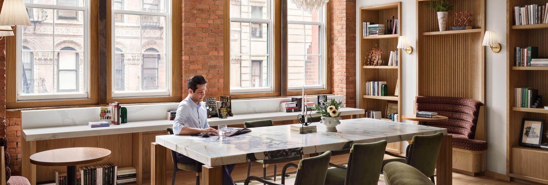Four people gathered around a long wood conference table in a meeting room with exposed brick, built-in shelving and a large colorful artwork.